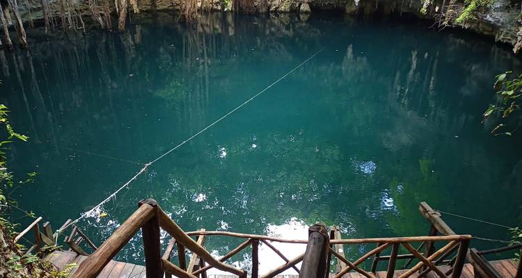 Cenote mit ruhigem Wasser, umgeben von Holzgeländern und Bäumen.