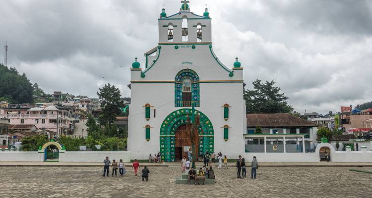 Weiße Kirche mit farbigen Akzenten, Menschen gehen über den Platz.