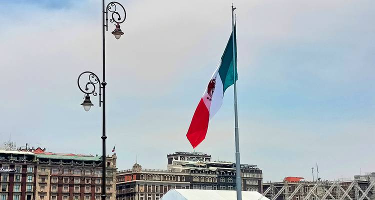 Mexikanische Flagge weht in einer Stadtlandschaft mit Gebäuden im Hintergrund.