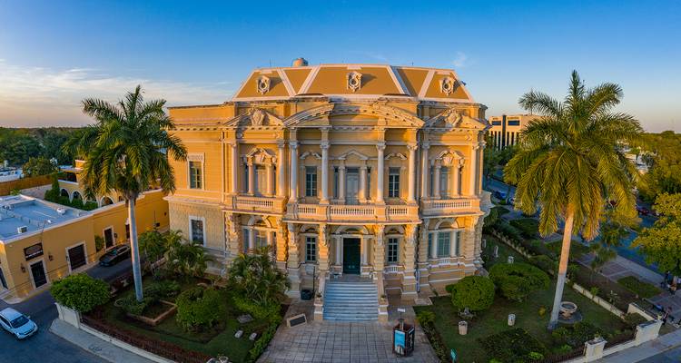 Großes historisches Gebäude mit Palmen unter blauem Himmel.