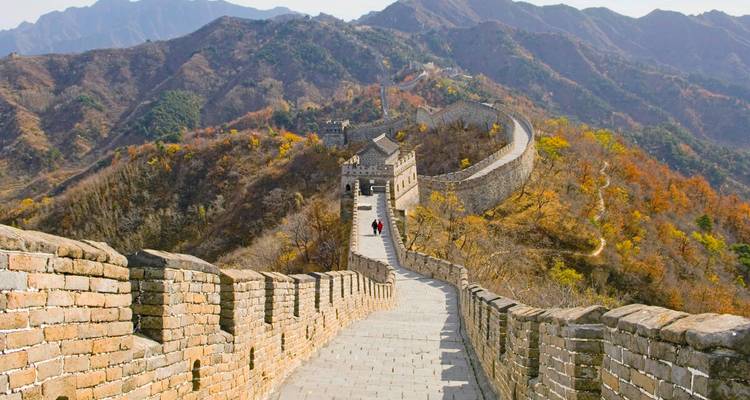 Steinerner Gehweg oben auf der Chinesischen Mauer, die sich über farbenfrohe Herbsthügel erstreckt.