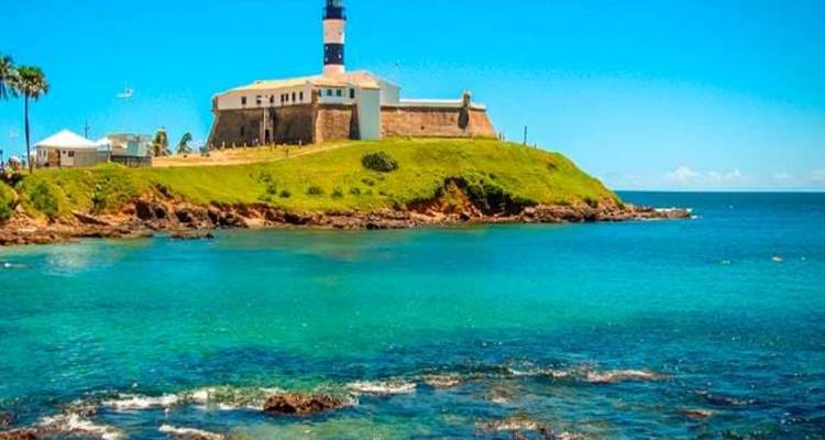 Lighthouse on a hill above clear blue waters.