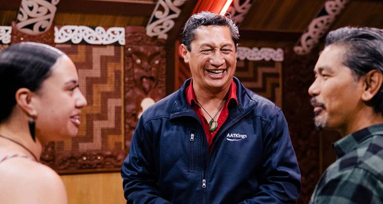 Three people in traditional Maori setting, smiling and conversing.
