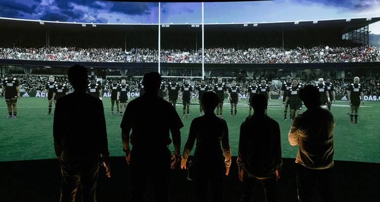 Menschen als Silhouetten beim Betrachten einer Rugby-Haka-Aufführung auf einem Bildschirm.