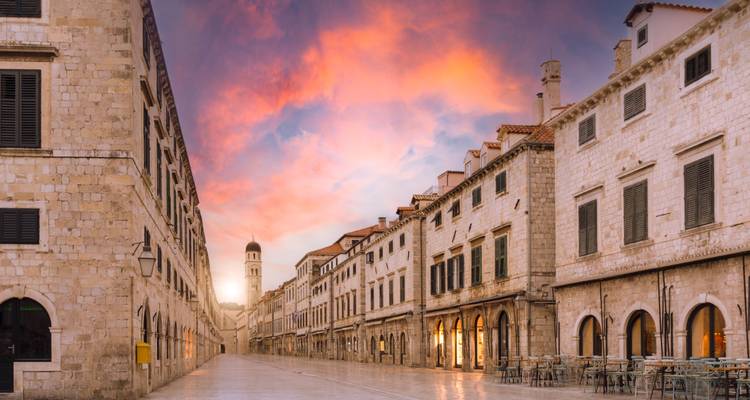 Historische straat met stenen gebouwen en een klokkentoren onder een kleurrijke hemel.