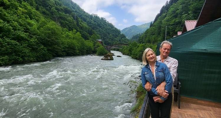 Paar posiert an einem Fluss mit einer üppig grünen Landschaft.