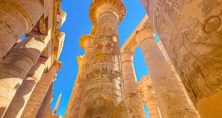 Interior view of a columned hall with ancient carvings and bright blue sky.