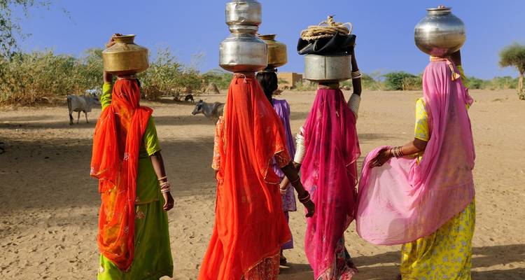Gruppe von Frauen, die Töpfe auf dem Kopf tragen in ländlicher Umgebung.