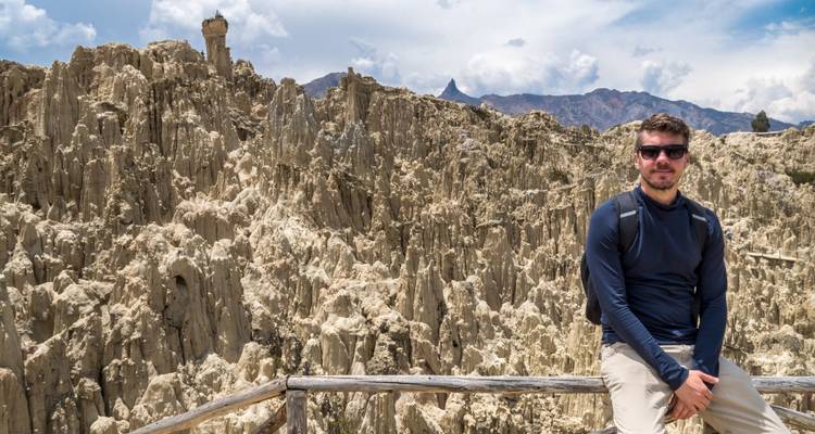 Man sitting on a wooden rail overlooking spired rock formations.