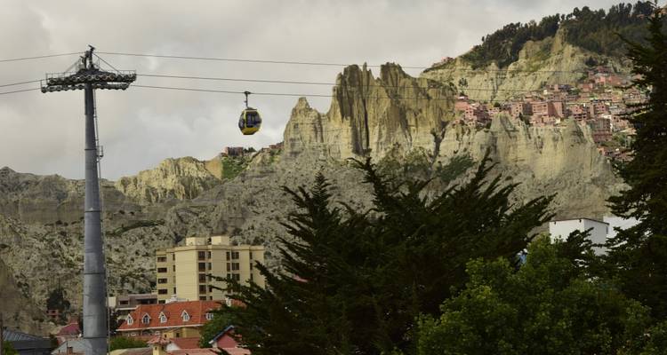 Cable car moving over a city with dramatic rock formations in the background.