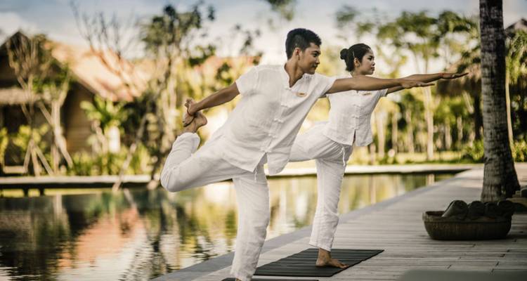 Couple pratiquant le yoga au bord d'une piscine sereine, entouré d'une végétation luxuriante.