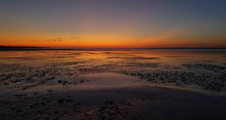 Un coucher de soleil coloré au-dessus d'une vaste plage avec des reflets sur le sable mouillé.