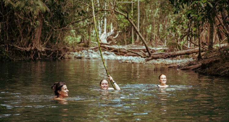 Trois personnes nageant dans une rivière entourée d'une végétation luxuriante.