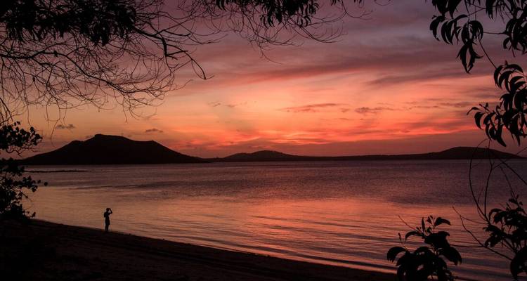Silhouette d'une personne sur une plage regardant le coucher de soleil sur l'océan.