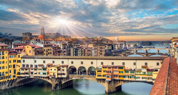 Los rayos de sol se abren paso entre las nubes sobre el Ponte Vecchio de Florencia y el río Arno, iluminando los coloridos edificios a orillas del río.