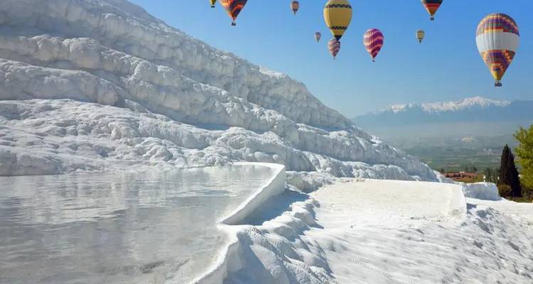Hot air balloons flying over the white terraces with a mountainous backdrop.