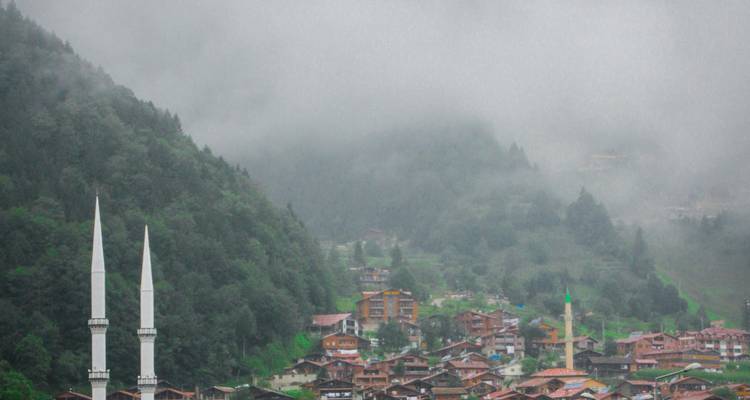 A misty view of a village with a mosque in a mountainous area.