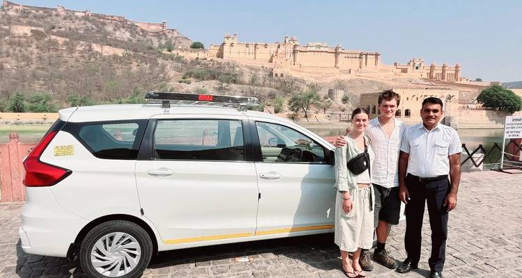 Turistas posando frente al Fuerte de Ámbar en Jaipur, India con un automóvil en primer plano.