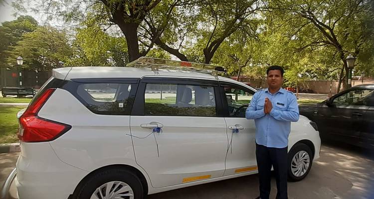 Hombre posando con un carro blanco bajo un árbol.