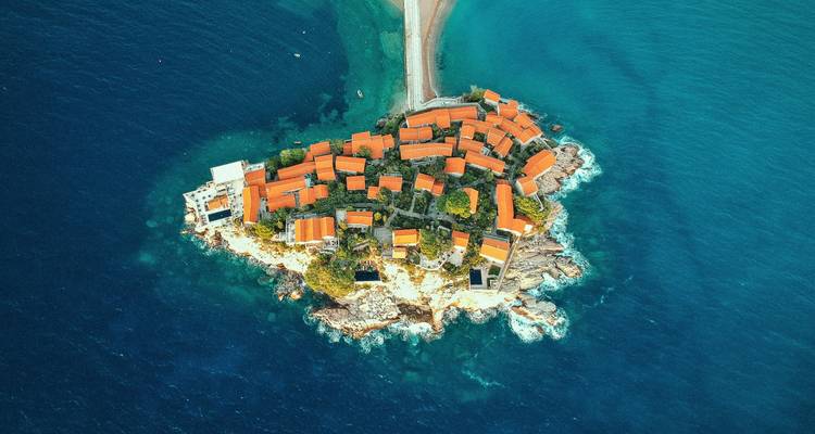 Luftaufnahme einer Insel mit rotgedeckten Gebäuden, umgeben von blauem Wasser.