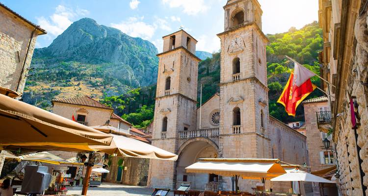 Eine historische Kathedrale mit Zwillingstürmen auf einem Platz, mit Menschen und Sonnenschirmen.