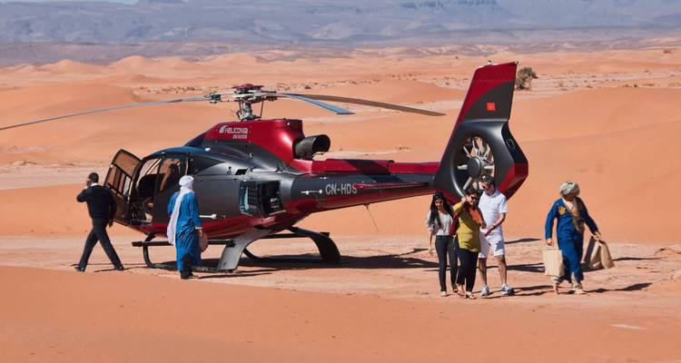 Group of people beside a helicopter on sand dunes in a desert landscape.