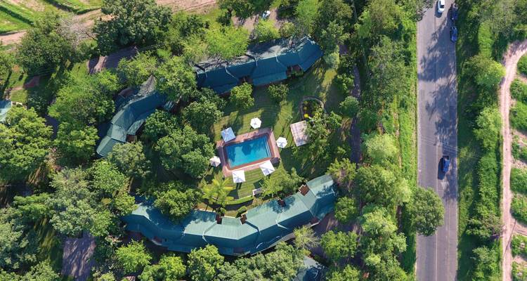 Vista aérea de un alojamiento circular escondido entre árboles frondosos con una piscina central y cabañas alrededor.