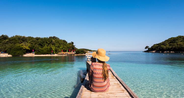 Woman sitting on a wooden pier overlooking clear blue water.