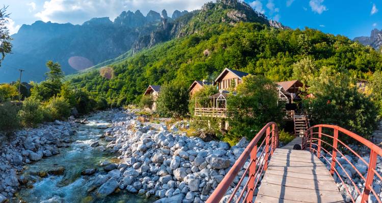 Malerische Aussicht auf einen Fluss, eine Holzbrücke und Berge.
