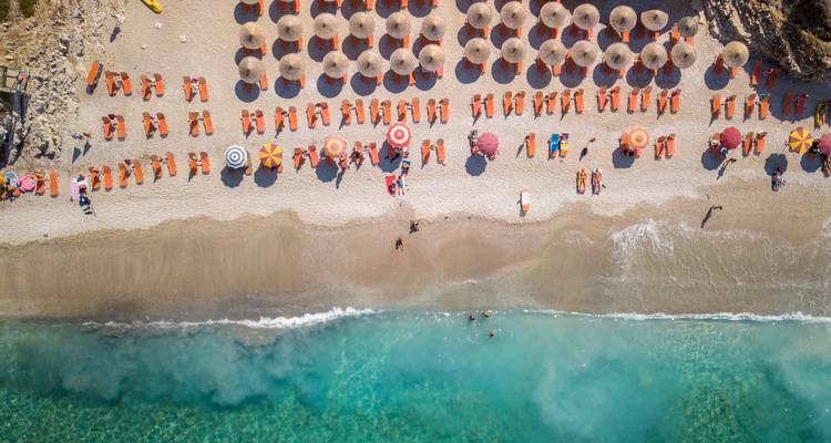 Luftaufnahme eines Strandes mit Sonnenschirmen und Strandbesuchern.