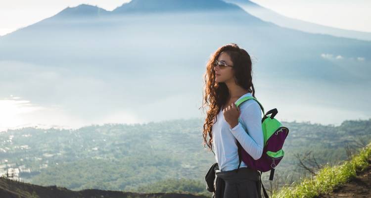 Woman standing in front of a mountainous backdrop with a backpack.