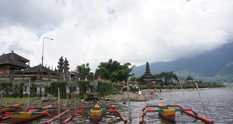 Temple on a lake with overcast sky and colorful boats.