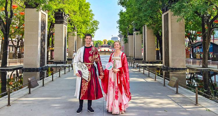 Couple in traditional attire holding fans, standing in a decorated pathway.