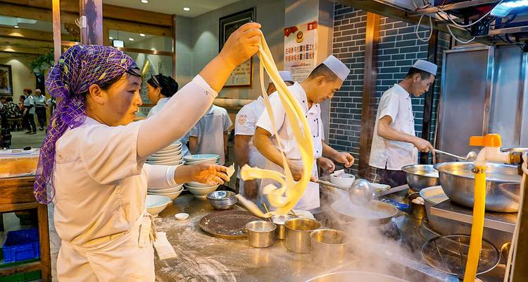 Chefs in a restaurant preparing traditional noodles.