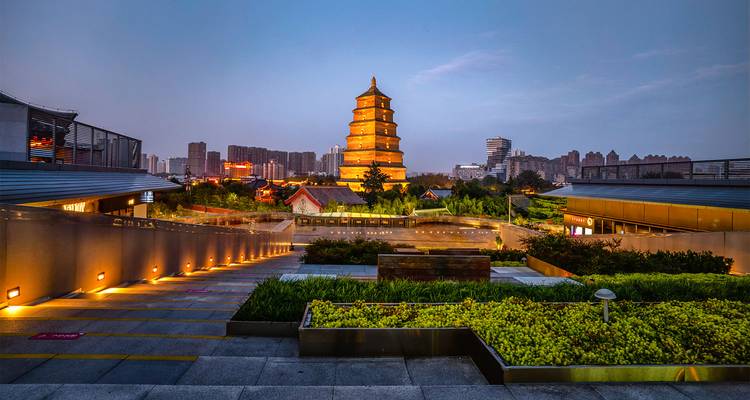 Complejo de la Pagoda de la Oca Salvaje Gigante iluminado al atardecer con el horizonte moderno de Xi'an de fondo.