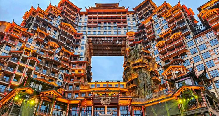 Complejo moderno enorme e iluminado de manera ornada con balcones apilados y un puente elevado central que brilla contra el cielo del atardecer.