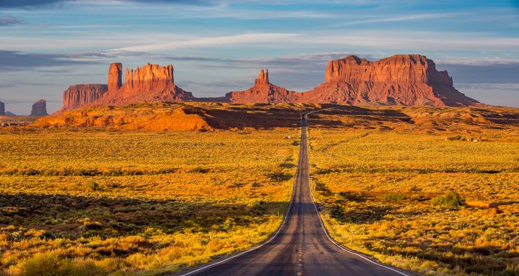 Larga carretera recta que conduce a grandes formaciones rocosas en un vasto desierto.