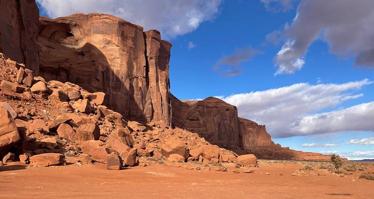 Senkrechte rote Felswände und verstreute Felsblöcke unter einem leuchtend blauen Himmel im Monument Valley.