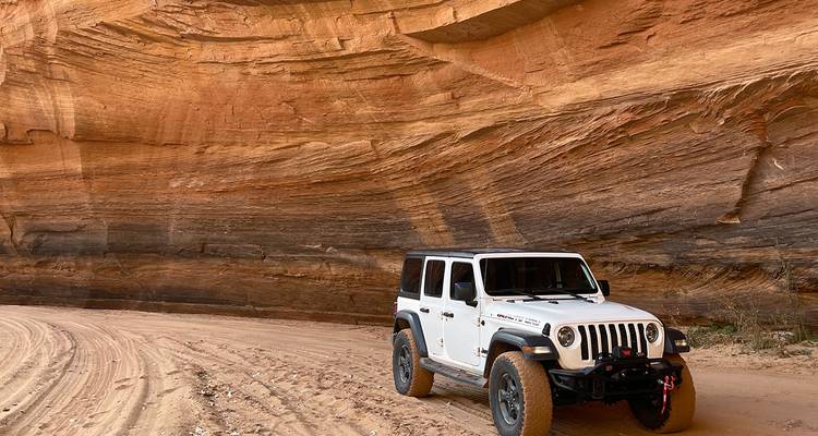 Weißer Jeep steht in einem dramatischen Sandsteinkanuon mit ausholenden, geschwungenen Gesteinsschichten.