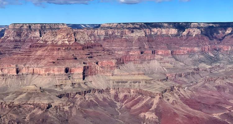Ausgedehnte mehrfarbige Schichten des Grand Canyon, die sich unter einem klaren blauen Himmel offenbaren.