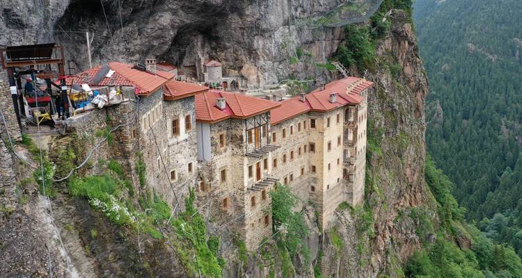 Monastery built into a cliff with tourists in view.