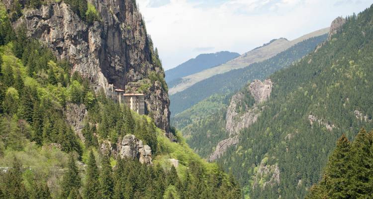 A lush green valley with a monastery built into the cliffside.
