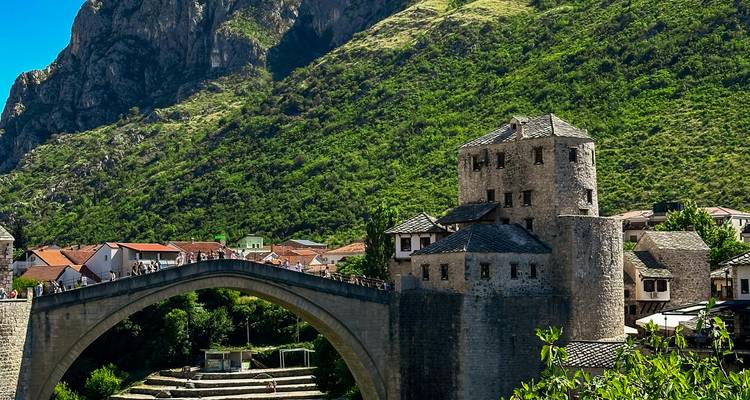 A stone bridge and medieval tower with mountains in the background.