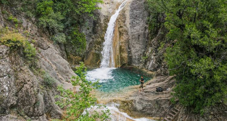 A waterfall cascading into a clear pool, person standing nearby.