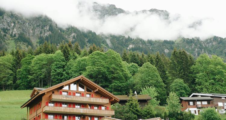 An alpine house with mountains and clouds in the background.