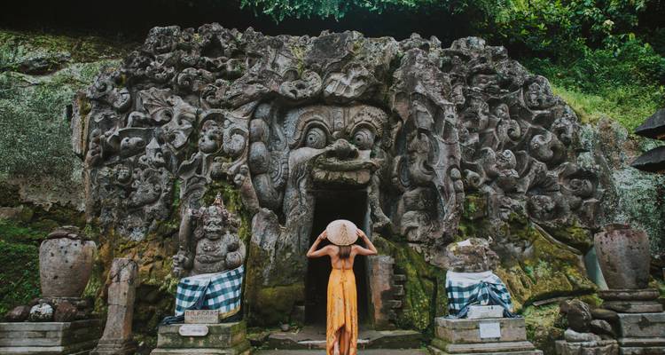 Personne debout à l'entrée d'une grotte de pierre ancienne ornementée.