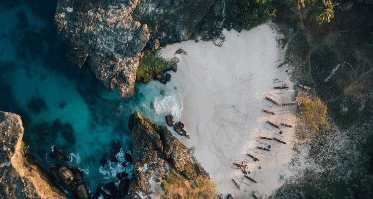 Vue aérienne d'une plage isolée avec des eaux claires et des falaises rocheuses.