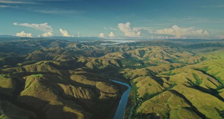 Vue aérienne d'une rivière sinueuse traversant des collines vallonnées sous un ciel bleu.