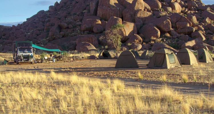 Tentes de camping dans un cadre désertique avec un arrière-plan rocheux.