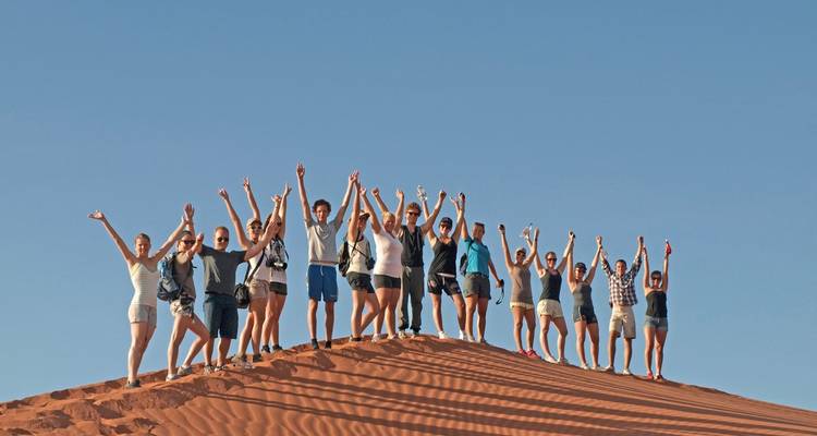 Grand groupe de personnes avec les bras levés sur une dune de sable.